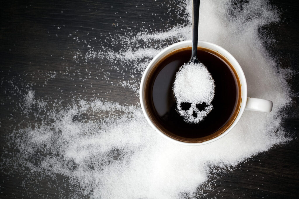 Unhealthy white sugar concept. Skull spoon with sugar and cup of black coffee