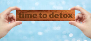 Hands holding a wood engrave with word "time to detox"