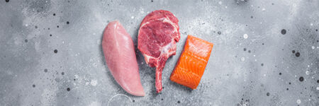 Chicken breast, steak, and salmon on slate background