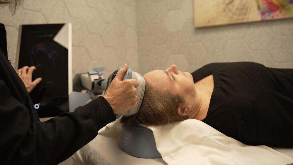 Denise holding Exomind TMS device to users head while checking progress